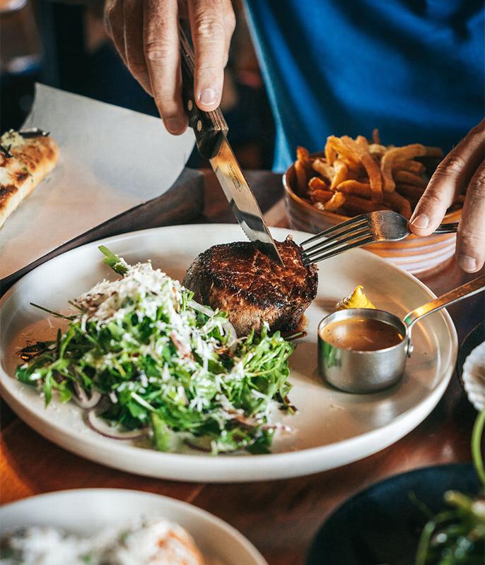 man cutting up steak on a plate in a restaurant